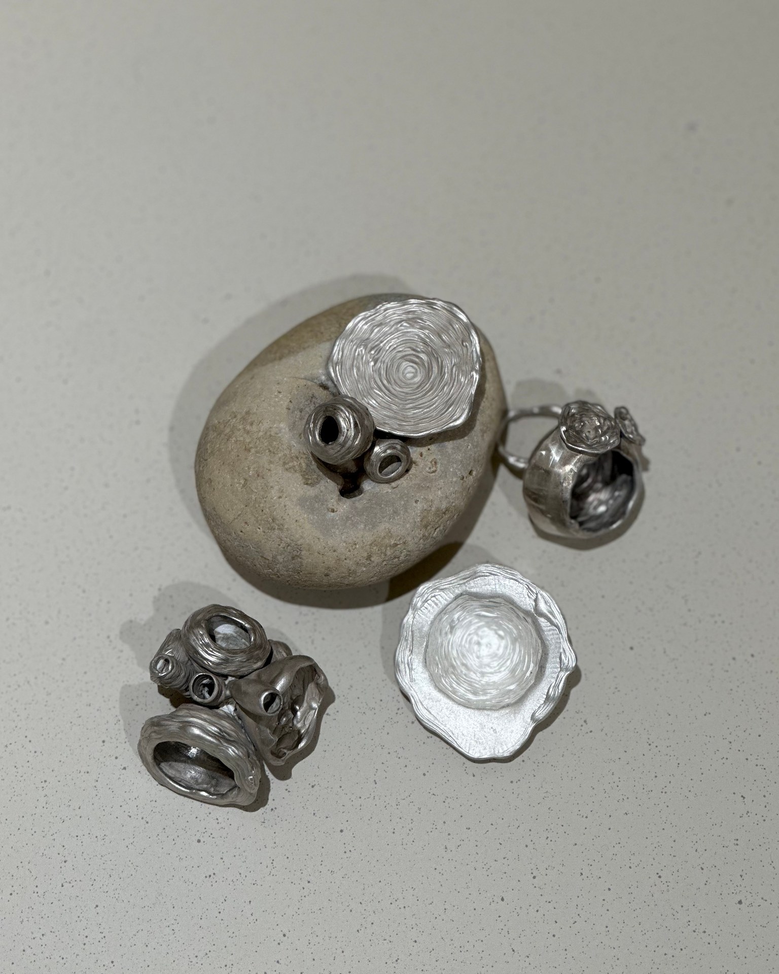 Silver jewellery arranged around a stone, with layered circular and organic forms.